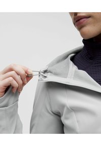 Chaqueta gris claro con cremallera, con un forro interior suave. Primer plano de una mano ajustando el tirador ajustable cerca del cuello.