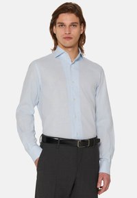 Svijetloplava košulja s dugim rukavima od glatke tkanine, s oštrim ovratnikom i uskim krojem, u kombinaciji s tamnim elegantnim hlačama.