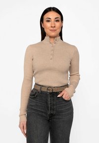 Maglione beige a costine a maniche lunghe con colletto alto e cinque bottoni, abbinato a jeans scuri a vita alta e una cintura grigia con fibbia rotonda.