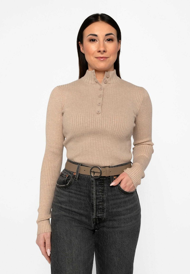 Maglione beige a costine a maniche lunghe con colletto alto e cinque bottoni, abbinato a jeans scuri a vita alta e una cintura grigia con fibbia rotonda.