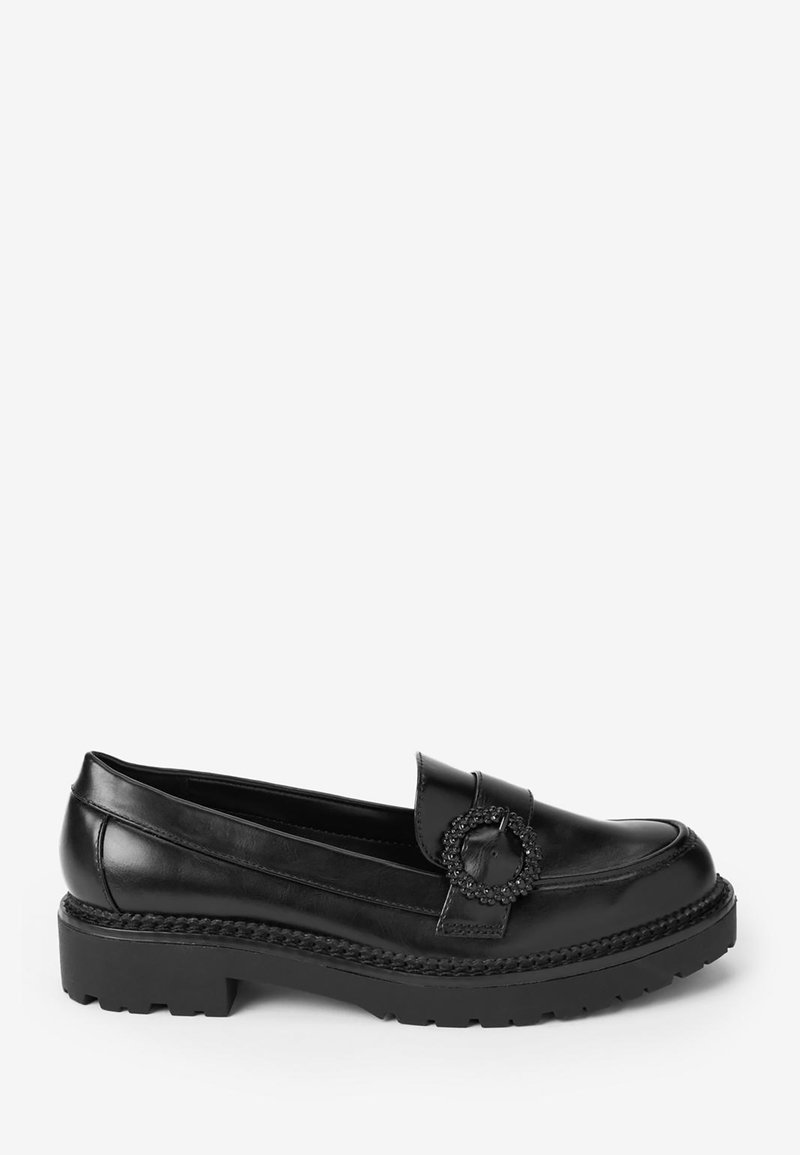 Mocassin en cuir noir avec semelle épaisse et boucle ronde décorative sur la bride supérieure, présenté en profil latéral sur fond blanc.