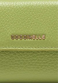 Zielony portfel z fakturowanej skóry, z wytłoczonym złotym logo "COCCINELLE" z przodu. Minimalistyczny design z przeszyciami na bokach.