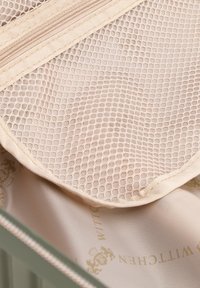 Beige gaasrits zakje binnenin een groene koffer, met een soepele textuur en een subtiele geprinte voering met lichtgroene accenten.