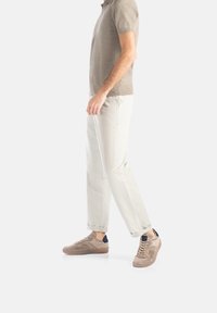 Beige Strick-Polohemd, cremefarbene Slim-Fit-Hosen und strukturierte beige Sneakers mit dunkelblauen Akzenten, getragen von einer Person, die geht.