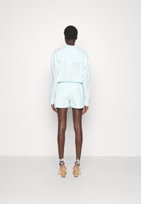 Outfit composto da una maglietta e pantaloni corti di un leggero colore menta. La maglietta presenta un falso colletto e maniche lunghe, mentre i pantaloni corti sono realizzati con una vestibilità comoda e rilassata.