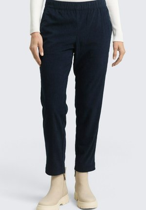 Granatowe prążkowane spodnie z elastycznym paskiem, o zwężanych nogawkach, zestawione z kremowymi botkami za kostkę. Teksturowana tkanina z pionowymi paskami.