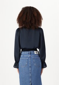 Mornarska satenasta bluza s napihnjenimi rokavi in zbranim koncem, v kombinaciji z visokim denim krilom z etiketom in hrbtnimi žepi.