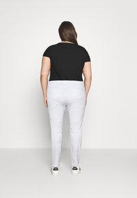 Top negro de manga corta combinado con pantalones ajustados de color gris claro, que cuentan con bolsillos traseros. La modelo lleva zapatillas blancas con detalles en negro.
