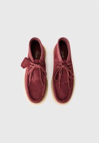 Et par bordeaux nubuck Clarks-sko med beige gummisåler og snørebånd, vist side om side på en hvit bakgrunn.