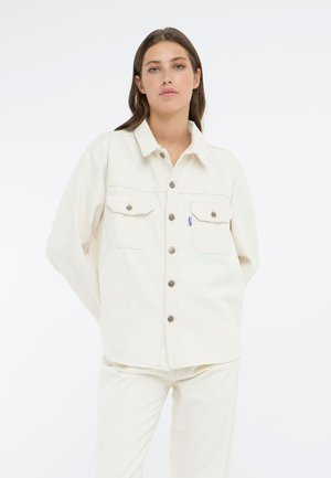 White denim jacket with a button-up front, large chest pockets, and a classic collar. The fabric is smooth with a slightly structured fit.