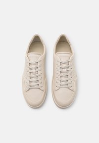 Jasnobeżowe sneakersy wykonane z gładkiej skóry mają zaokrąglony czubek, płaskie sznurówki i subtelne logo w okolicy języka. Czysty design całości.