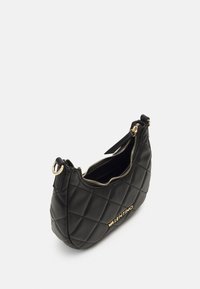 Black quilted leather shoulder bag with gold hardware. Zipper closure, rounded shape, and logo detail on the front. Textured finish.