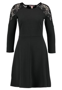 Czarna sukienka z długimi rękawami; posiada koronkowe akcenty na ramionach, dopasowane bodice oraz rozkloszowany dół. Wykonana z gładkiego, miękkiego materiału.