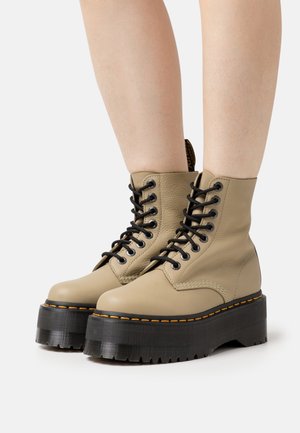 Beige Leder-Ankle-Boots mit schwarzen Schnürsenkeln, ausgestattet mit einer robusten schwarzen gerippten Sohle und orangefarbenen Nähten entlang der Kante.