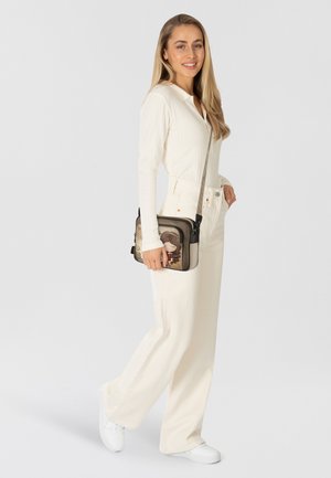 Umhängetasche mit dekorativem Design, das ein stilisiertes Gesicht zeigt, gefertigt aus weichem beigem Stoff und ergänzt durch einen schwarzen Reißverschluss und Riemen.