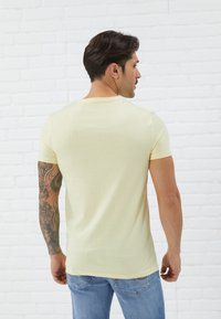 Light yellow short-sleeve t-shirt made of cotton, featuring a crew neck and a fitted design, worn with blue denim jeans.