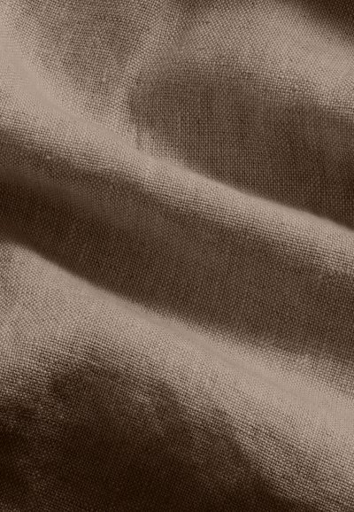 Gros plan d’un tissu beige texturé avec un tissage visible et des plis doux créant des ombres légères.