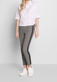 Vit kortärmad knäppskjorta, grå och svarta hundtandsmönstrade byxor med sidskärningar, och vita sneakers. Slät tyg, avslappnad passform, ruta mönster.