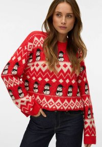 Roter Strickpullover mit weißen Schneemann- und Rautenmuster, strukturierter Stoff, Rundhalsausschnitt und langen Ärmeln. Kombiniert mit dunklen Jeans.