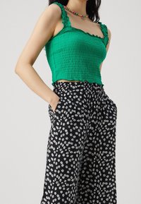 Zielony top z falbanami na ramiączkach i marszczonym przodem, zestawiony z czarnymi spodniami w białe kwiaty i elastycznym paskiem w talii.