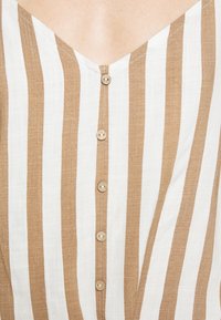 Brown and white striped top with a V-neck, featuring five circular buttons and a textured fabric. Buttons align down the center.