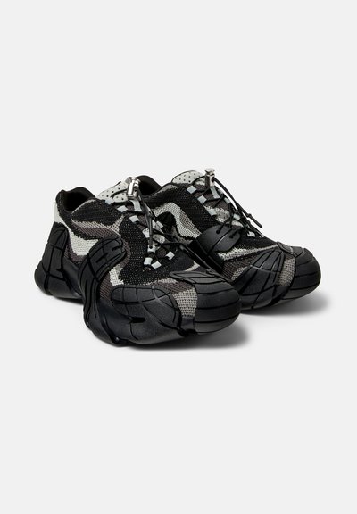 Svart och grå stickade sneakers med en strukturerad gummisul, justerbara snörningar och en distinkt formgiven design med vågiga mönster.