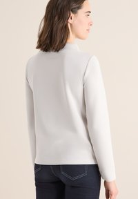 Lichtgrijze langemouwen top met een kraag, gladde textuur, getailleerd ontwerp en zijslitsen, gecombineerd met donkerblauwe spijkerbroek met ronde achterzakken.