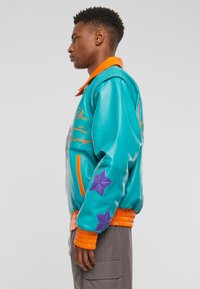 Tyrkysová kožená bomber bunda s oranžovým límcem a žebrovanými manžetami, s fialovými hvězdicovými akcenty na rukávech a vyšitými detaily.