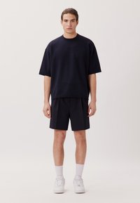 T-shirt oversize in tessuto navy abbinato a pantaloni corti coordinati. Il modello indossa sneakers bianche e calze bianche a lunghezza polpaccio. Design semplice e minimal.