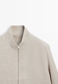 Light beige textured jacket with a standing collar and a front silver zipper, shown from the chest up against a white background.