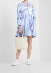 Gestreiftes Kleid in Hellblau und Weiß, mit langen Ärmeln und einem gestuften Rock. Kombiniert mit einer cremefarbenen Tasche und weißen Sneakers.