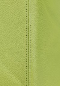 Textureret limegrøn lædermateriale med synlig syning langs sømmen, der viser en glat overflade og let kornmønster.
