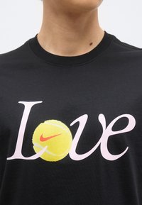 Μαύρο πουκάμισο με τη λέξη «Love», όπου το «o» έχει αντικατασταθεί από μια κίτρινη μπάλα τένις με κόκκινο λογότυπο Nike.