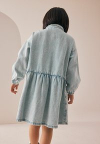 Abito di jeans azzurro chiaro con vita arricciata, maniche lunghe e vestibilità comoda. Presenta un colletto e una gonna leggermente svasata.
