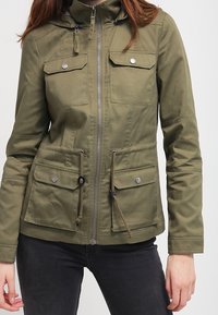 Olivově zelená zipová bunda s kapucí, která má dvě náprsní kapsy a nastavitelné stahování v pase, vyrobená z hladkého materiálu.