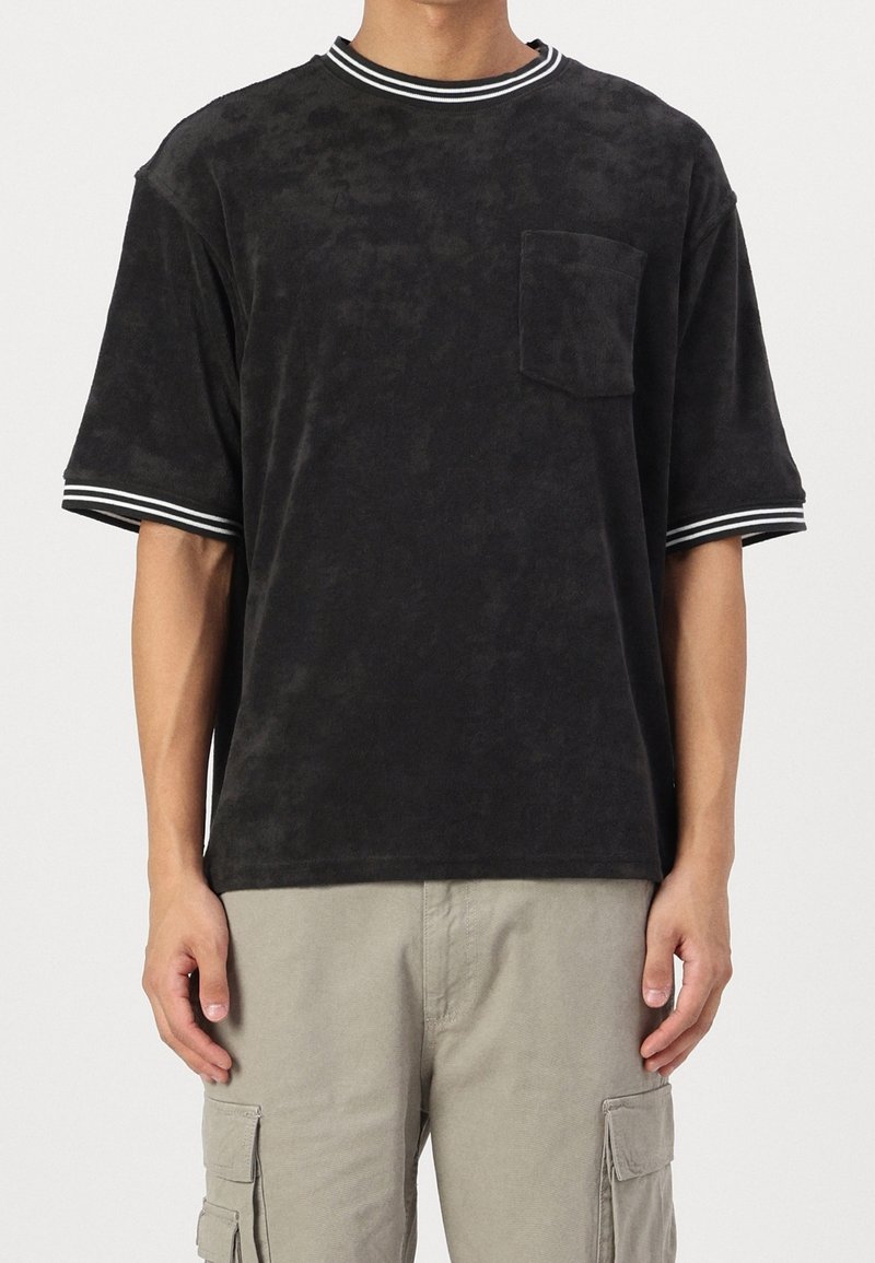 T-shirt noir à manches courtes en tissu doux, avec un col et des ourlets côtelés à rayures blanches, une poche poitrine et une coupe décontractée.