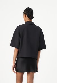 Maglietta nera a maniche corte con colletto, realizzata in tessuto strutturato. Indossata con una minigonna nera coordinata, che mostra una superficie liscia e linee pulite.