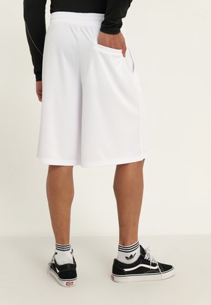Weiße Sportshorts mit strukturierter Oberfläche, elastischem Bund und Seitentaschen. Kombiniert mit schwarzen Turnschuhen und gestreiften Socken.