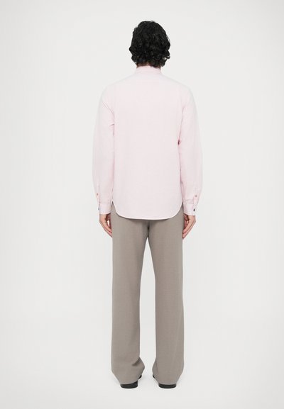 Cămașă roz pal cu mâneci lungi și tiv rotunjit, asortată cu pantaloni gri. Nasturii de la manșete sunt detaliați cu culori contrastante.