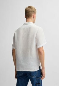 Witte linnen shirt met korte mouwen en een ontspannen kraag, met een licht gestructureerd oppervlak en opgerolde manchetten, gezien van achteren.