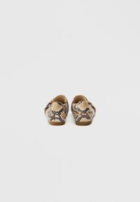 Ballerines à motif peau de serpent avec un embout arrondi, dotées d'une semelle couleur noisette et d'une texture douce, vues de dos sur un fond clair.