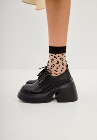 Black lace-up shoes with a chunky heel and cut-out design, paired with leopard print sheer ankle socks featuring a black band.