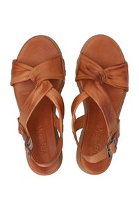 Bruine sandalen met gedraaide banden en een enkelgesp, van bovenaf gepositioneerd op een effen achtergrond. Merknamen zijn zichtbaar op de zool.