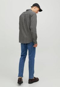 Camisa de cuadros de manga larga en negro y gris, corte relajado, con cuello abotonado, combinada con pantalones vaqueros azules y zapatos marrones.