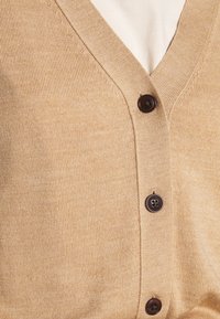 Beige kofta i ribbstickat material med V-ringning och mörkbruna knappar. Har en mjuk textur och klassisk passform.