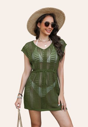 Abito coprente in crochet verde oliva, maniche corte, scollatura a V, vita con cordoncino, con motivi a maglia aperta e sovrapposto a un costume da bagno.