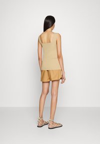 Beige ribbad linne med fyrkantig halsringning och tjocka axelband, kombinerat med ljusbruna veckade shorts och remsandaler.