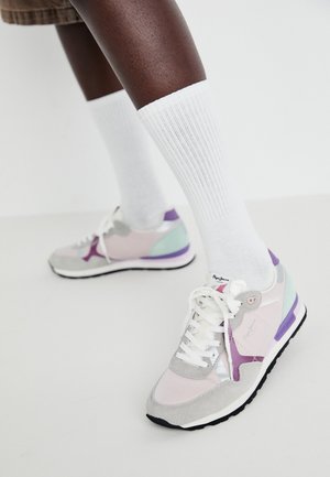 Piernas con calcetines crew de canalé blancos y zapatillas de colores pastel con cordones blancos sobre un fondo claro y liso.