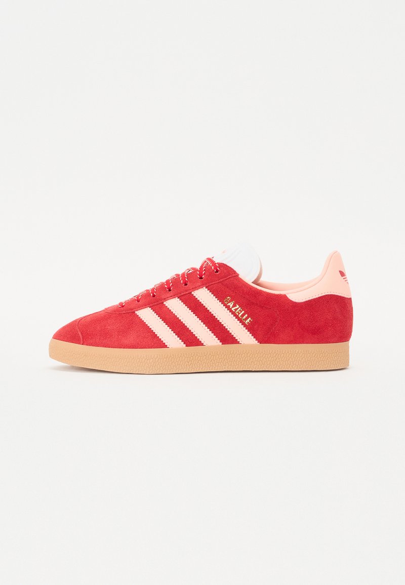 Red suede sneaker with light pink accents, three white stripes, gum sole, and branded logo. Low profile and lace-up design.