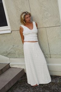 Haut blanc sans manches avec un motif floral texturé, associé à une longue jupe blanche fluide arborant un design en grille et une taille à cordon.